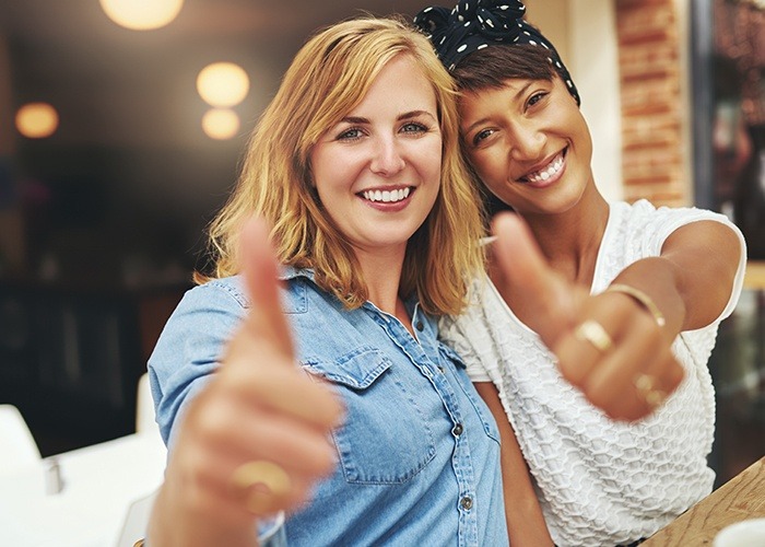 Two smiling women giving thumbs up after cosmetic dentistry