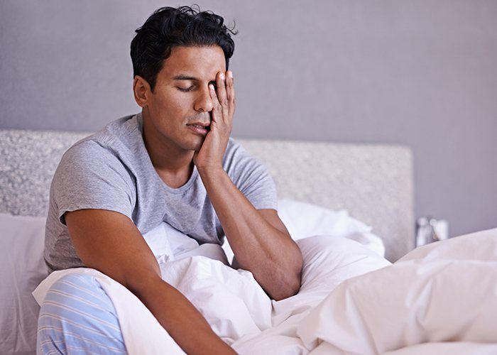 Tired man in need of sleep apnea therapy frustrated with head in hands