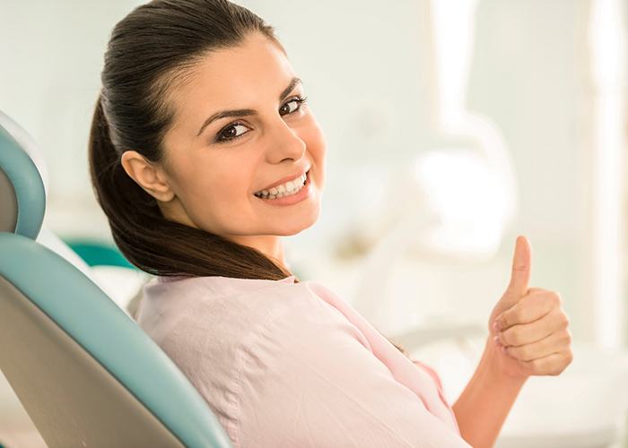 Female dental patient in light pink shirt giving thumbs up