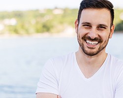 Man in a white shirt smiling in front of a lake