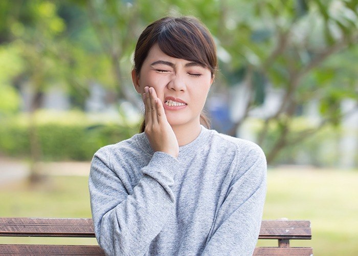 Woman in pain holding cheek in need of emergency dentistry