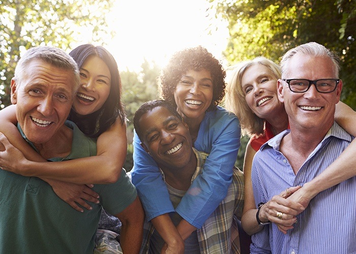 Six older men and women smiling outdoors after restorative dentistry