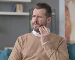 Man sitting on sofa, suffering from toothache