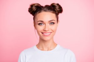 girl with space buns smiling with a pink background 