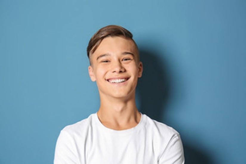 teen in white shirt smiling on blue background