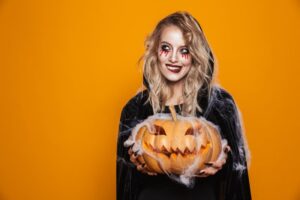 Woman in a Halloween costume smiling while holding a pumpkin